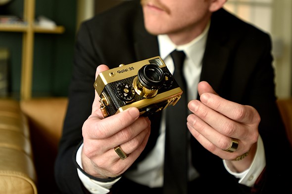 Man in suit holding a gold-plated Retrospekt Rollei 35 camera