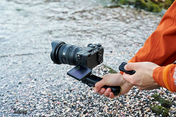 a hand holds a camera by an attached grip while other hand holds a remote