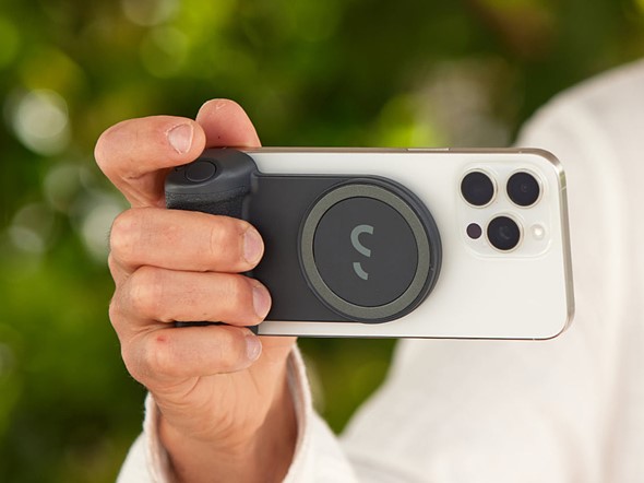 a hand holds a phone with grip attached against blurred green background