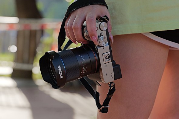 a hand holds camera with laowa wide angle macro lens in front of blurred background