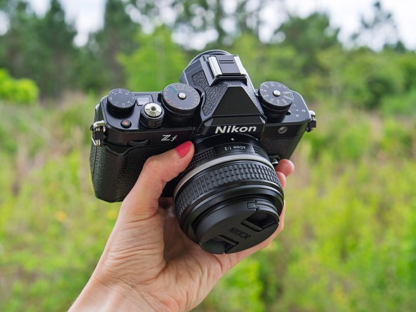 a hand holds nikon camera with 40mm lens in front of green forest