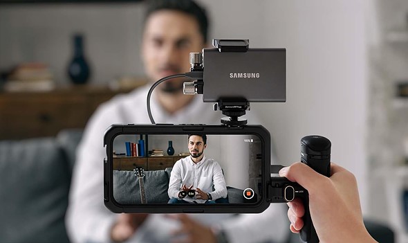 a hand holds smartphone with grip and ssd on top while recording video of man