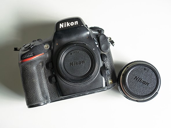 a nikon d800 sits next to lens on white desk