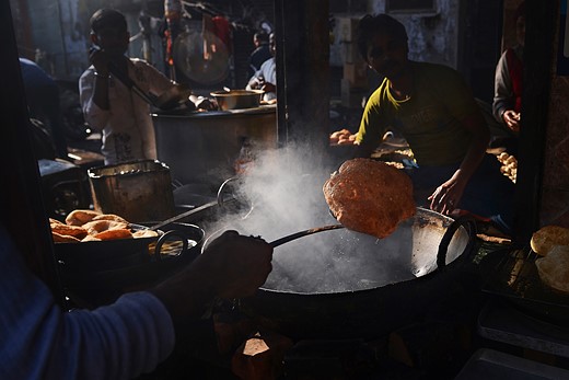 a person scoops Pooris out of vat in busy street market