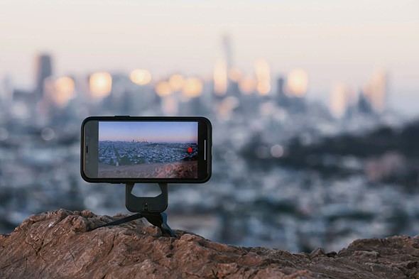 a tipod holds smartphone on rocks overlooking city