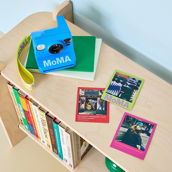 blue moma polaroid now camera on bookshelf with books and photos