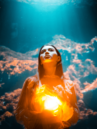 A woman holding a glowing orange orb against a deep blue underwater backdrop, embodying vibrant photography through dramatic lighting and color contrast.