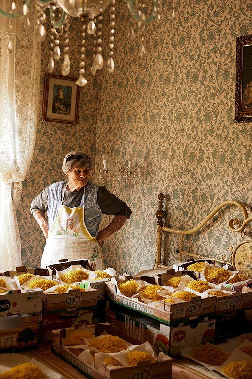 elderly woman stands in room looking at bags of pasta