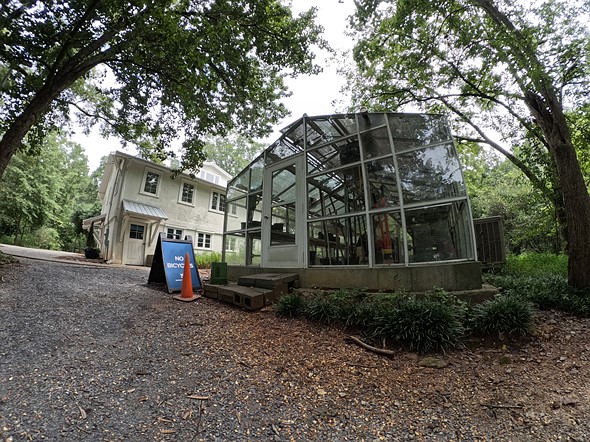 greenhouse next to house with large trees and gravel road