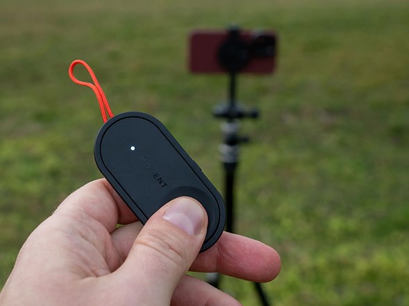 hand holds moment bluetooth remote in front of phone on tripod
