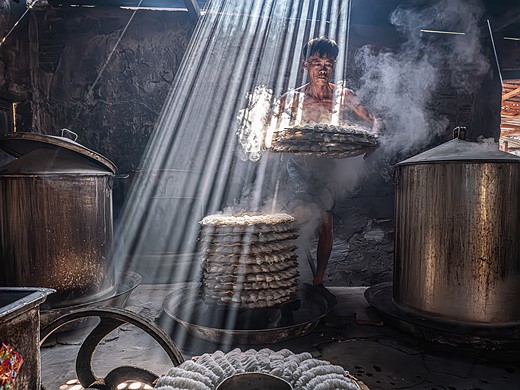 man carries tray of food in dark room with swirling smoke and beams of light