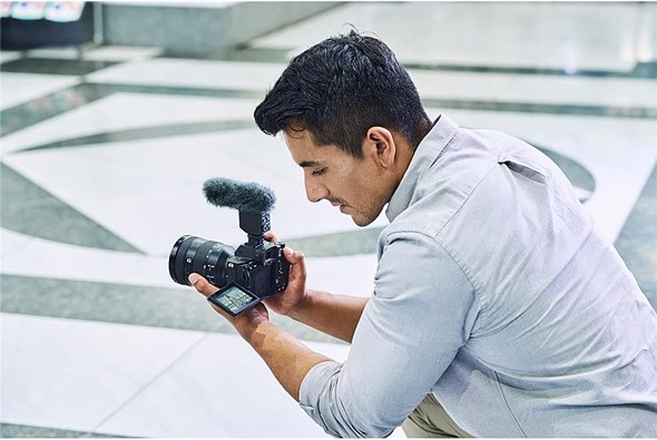 man holds sony 17 iv with mic with blurred background