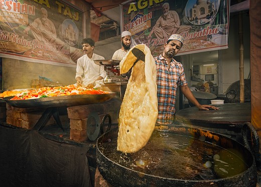 man pulls a large bread out of pan in street food stall