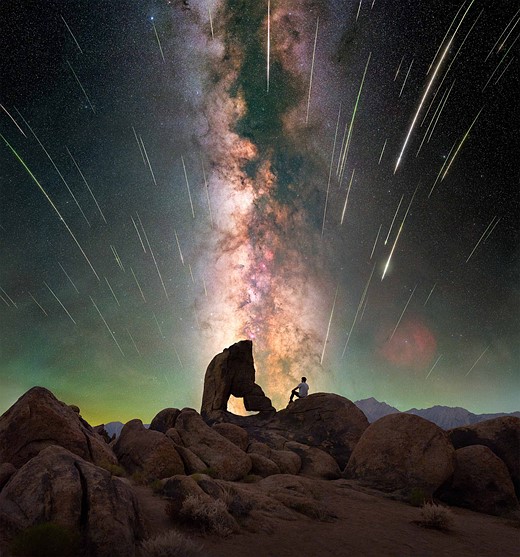 person sits on rock in front of natural arch and milky way