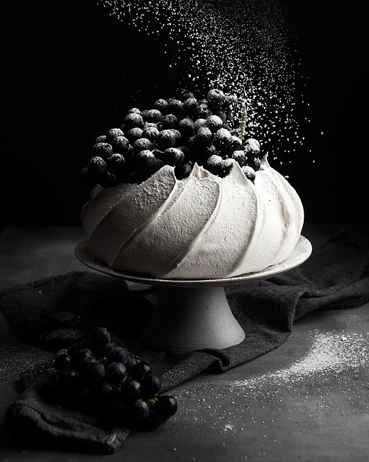 powdered sugar sprinkles over pavlova against dark background