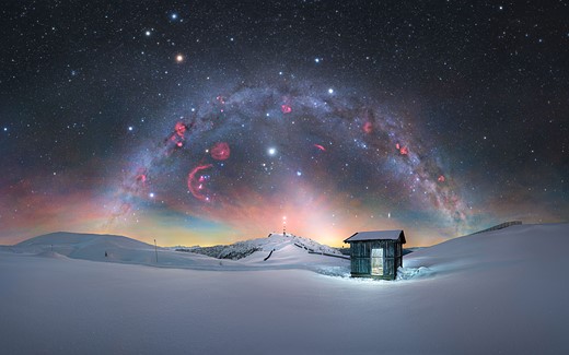 wood shed glows in winter scene with colorful milky way overhead