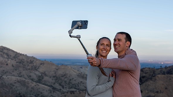a couple poses in front of overlook while one holds a selfie stick with a phone at arms length