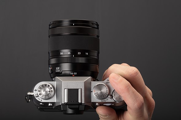 a hand holds a silver mirrorless camera with black background