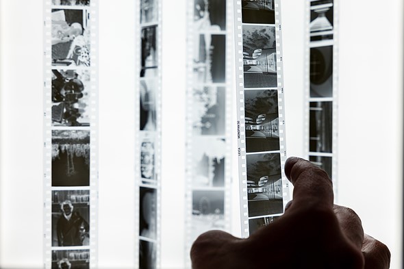 a hand reaches out to a row of negative strips hanging in front of light box