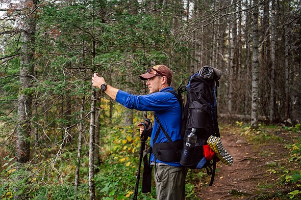 a person with a backpack holds their phone at arms length while in a forest