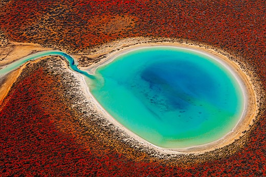 a turquoise body of water is surrounded by red earth