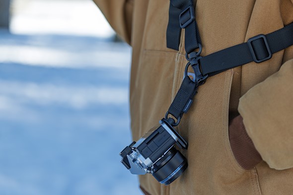 camera hangs from camera strap on person wearing brown jacket