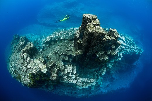 columns of basalt stick out of blue water with diver above