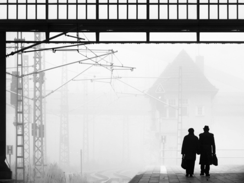 Tonal extremes black-and-white photography of two people walking side-by-side in foggy train station, with silhouettes and diffused light enhancing the scene.