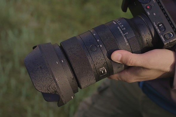 hand holds sigma lens speckled with water over blured green background