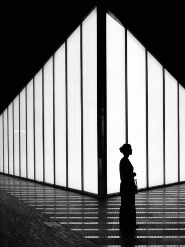 Tonal extremes in black-and-white photography showing a silhouetted woman standing near a large illuminated window, creating strong contrast and dramatic effect.