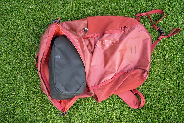 a black camera instert sits partially inside a red backpack placed on green turf