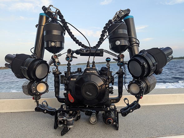 a camera in underwater housing with lots of attachments sits in front of water