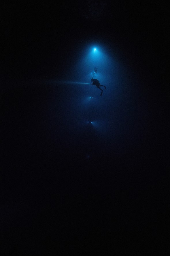 a diver floats next to a vertical line of lights in dark water