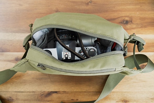 a green sling sits open on a wood table with an old camera inside