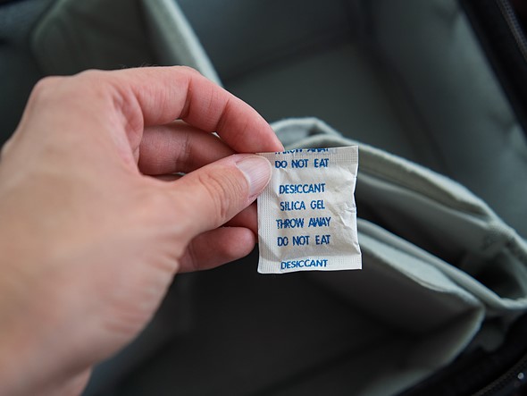 a hand holds a silica gel pack over a camera bag