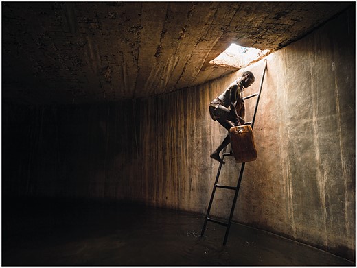 a person climbs down a ladder with a jug into a dark room filled with water 