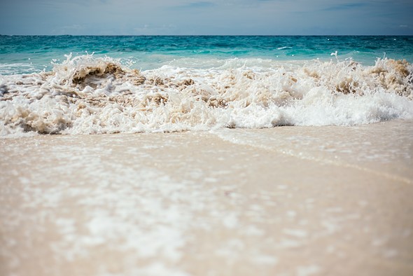 a small wave washes into a beach with vibrant blue water behind it
