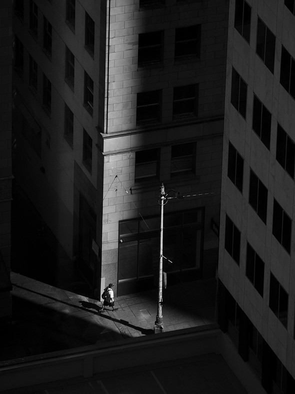 a streak of sun illuminates a building corner and person walking on the street