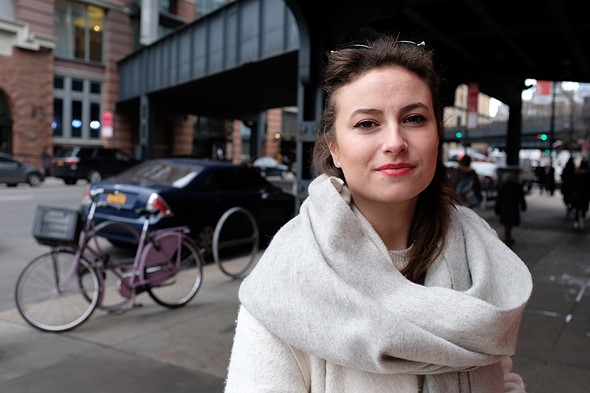 a woman wearing a large white scarf smiles lightly on a sidewalk in a city