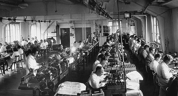 rows of desks with people working fill a large room