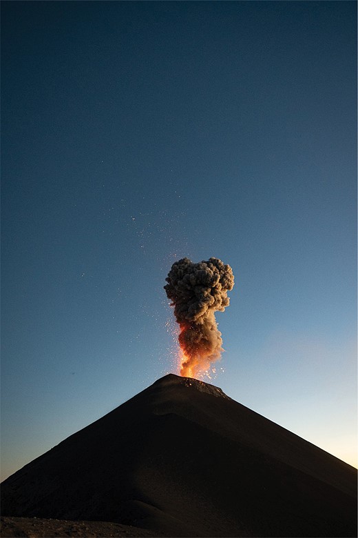 smoke and sparks spew out of a volcano with a clear dark blue sky