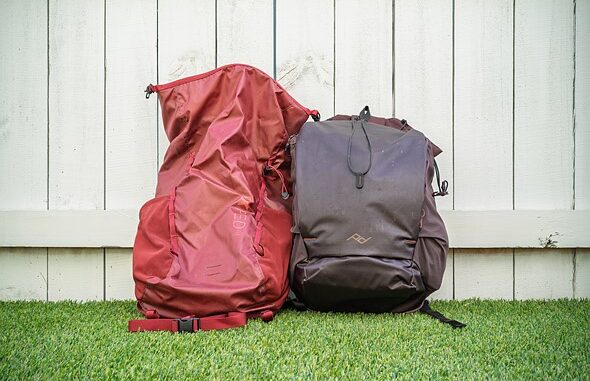two_backpacks_sit_against_a_white_fence_on_green_turf
