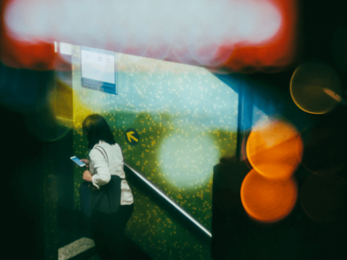 A woman on a stairwell using her phone, overlaid with colorful bokeh lights, created using in-camera multiple exposure for a dreamy, layered effect.