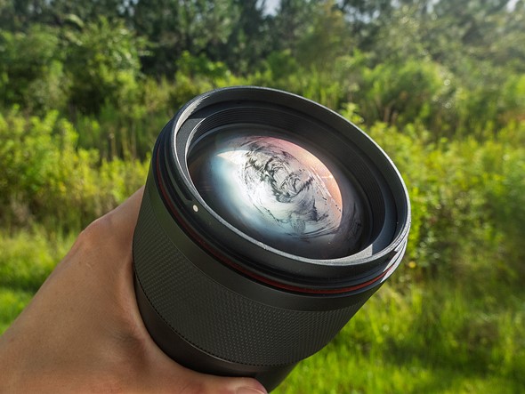 a hand holds a black lens that is fogged up in front of blurred grass