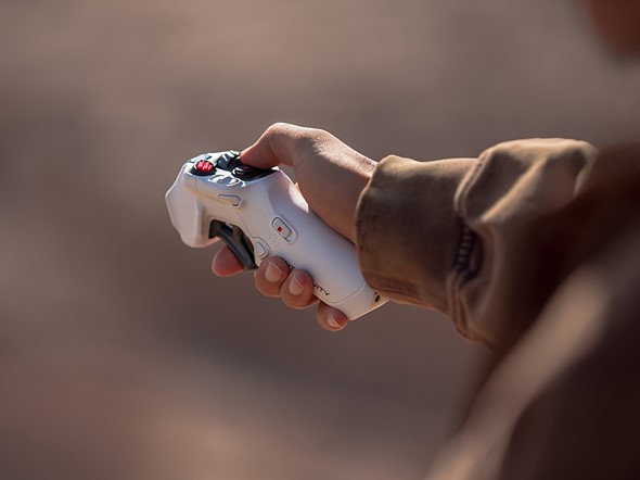 a hand holds a remote control over a blurred red dirt background