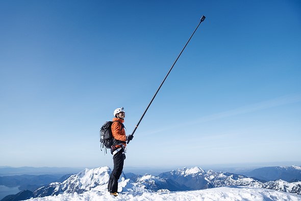 a man stands on a mountain covered in snow while holding a long selfie stick