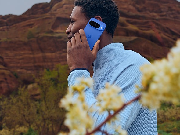 a person holds a blue phone to  their ear while walking in front of red cliffs