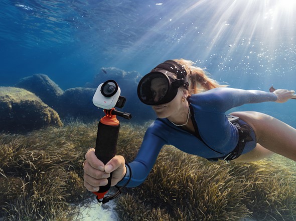 a person holds a camera attached to a float handle while underwater