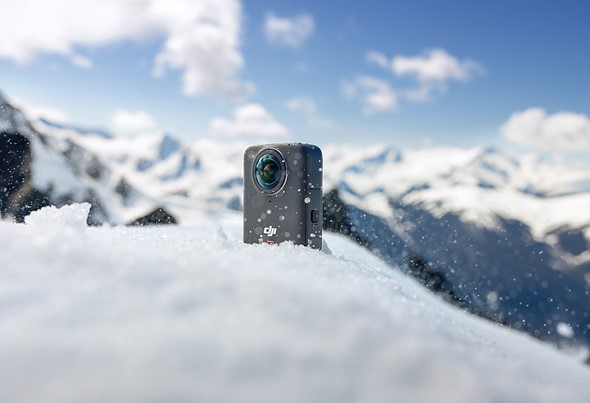 a small black 360 camera sits in snow on a mountain
