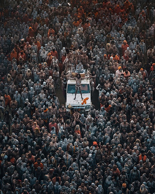 a white vehicle is surrounded by a large crowd of people earing orange and blue